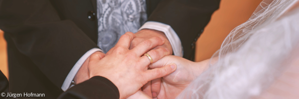 Hände von Braut und Bräutigam, die einander halten und von der Hand einer Pfarrperson bedeckt werden