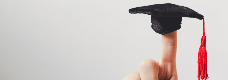 ein Miniatur-Doktorhut auf einem Zeigefinger