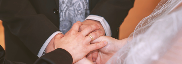 Hände von Braut und Bräutigam, die einander halten und von der Hand einer Pfarrperson bedeckt werden